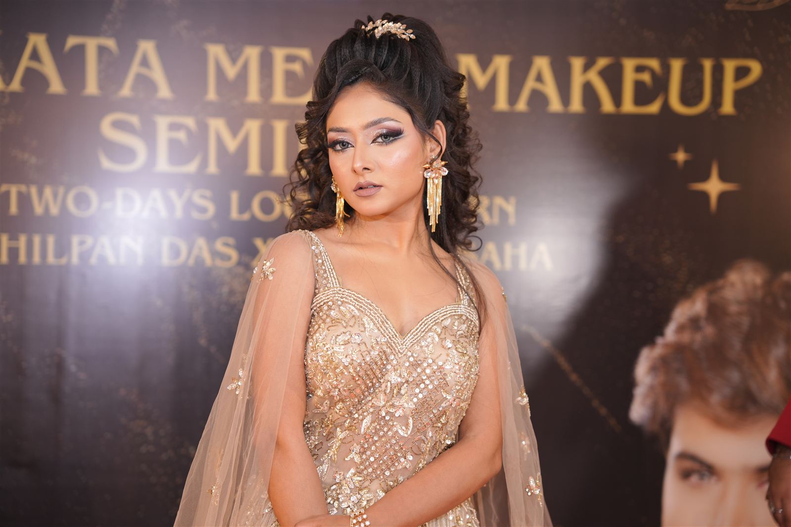 Model in a gold gown posing in front of the Kolkata Mega Makeup Seminar backdrop