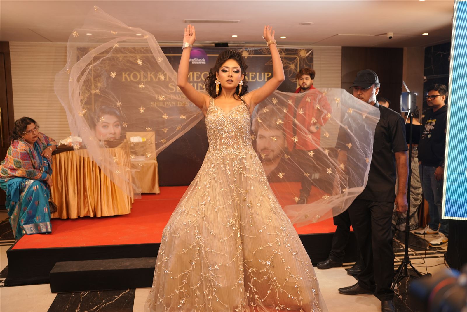 Model in a gold gown throwing her veil up on stage